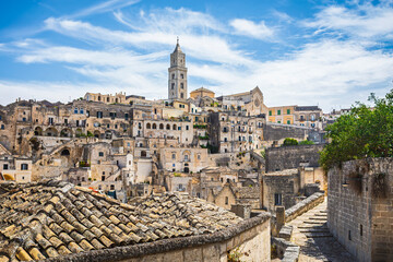 Obraz premium Daytime panoramic view of the historic town of Matera in southern Italy. The image highlights ancient stone houses, narrow streets, and the iconic Matera Cathedral rising above the Sassi cave dwelling