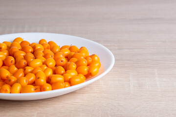 Ripe sea buckthorn in ceramic dish on wooden table, natural vitamins and healthy food, authentic.