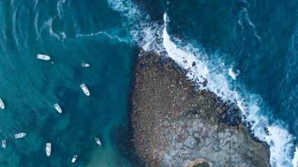 Aerial view of boats bobbing serenely in the tranquil turquoise waters contrasted against the rugged, wave-battered coastline, Sydney, New South Wales, Australia.