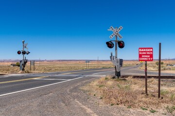 Rural railroad crossing with warning signs under a clear blue sky in a desert landscape.