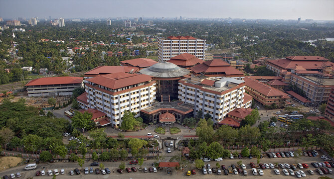 Aerial view of a sprawling building complex with striking red rooftops contrasting against the lush green landscape, Ponekkara Road, Kochi, Kerala, India.