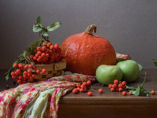 Autumn still life on the window - a bouquet of mountain ash, pumpkin, apples and a knitted blanket. Cozy house interior