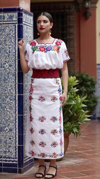 Beautiful Young Mexican Woman in Colorful Traditional Huipil Dress, Dancing Gracefully Near Historic Talavera Ceramic Tile Wall in Mexican Courtyard Setting, Cultural Fashion