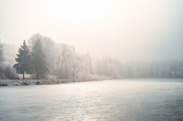 Magical winter landscape with a frozen lake, mist, and the gentle glow of Christmas sunlight