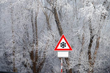 A warning sign with a large snowflake stands in a magical white winter landscape, alerting to...