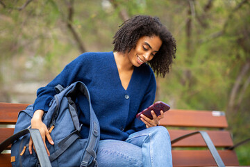 Happy young woman using smartphone on park bench