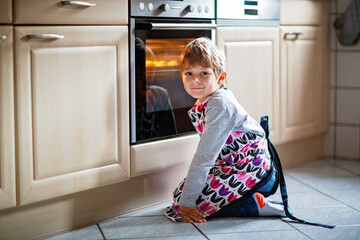 Cute blond boy baking muffins or pie in domestic kitchen. Happy child having fun with helping,...