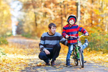 Little kid boy and his father in autumn park with a bicycle. Dad teaching his son biking