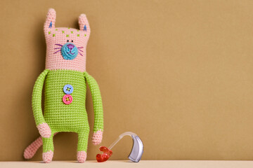 Colorful crocheted cat stands next to a hearing aid, highlighting innovative audiology solutions...