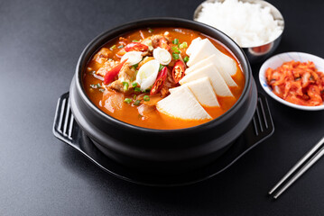 Korean food (Kimchi Jjigae), Kimchi soup with tofu, pork, scallion and chili in Korean stone bowl eating with cooked rice and kimchi on black background