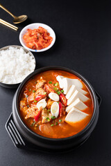 Korean food (Kimchi Jjigae), Kimchi soup with tofu, pork, scallion and chili in Korean stone bowl eating with cooked rice and kimchi on black background