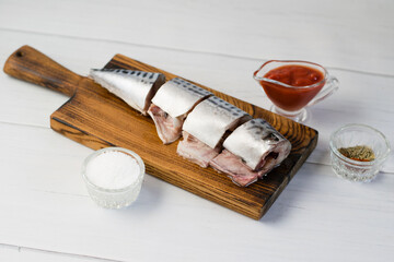 Raw mackerel fish on a cutting board, cooking fish with salt, spices and sauce