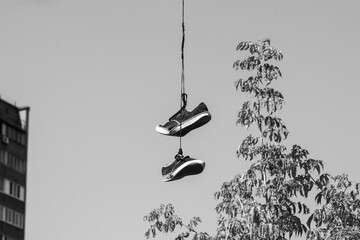 Pair of old sneakers hanging on an electric wire against a gray sky. Shoes hanging on wire