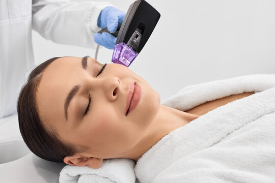 Woman while RF lifting procedure for her face skin tightening with cosmetologist at a beauty salon