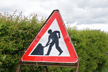Close Up of Triangular Metal Traffic Sign with Workman Logo seen against Green Hedge