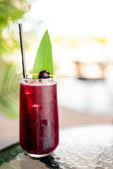 Refreshing iced cocktail with cherry, leaf garnish, and metal straw in a tall glass on outdoor...