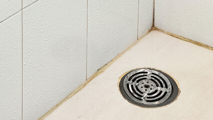 Stainless steel bathroom floor drain with water drops in washroom. Concept for hygiene, plumbing, drainage, cleaning, or maintenance