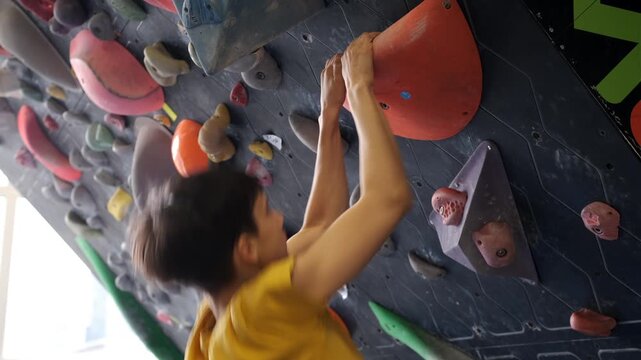 Closeup side view of a teenage boy doing pullups on a large sloper volume during climbing training on an indoor bouldering wall.