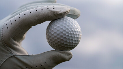 Close-Up Image of a Hand Holding a Golf Ball Against a Cloudy Sky