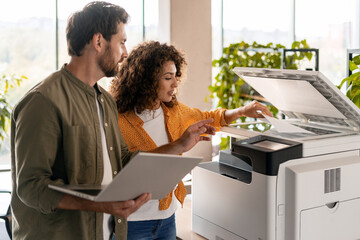 Business colleagues using printer in office with laptop