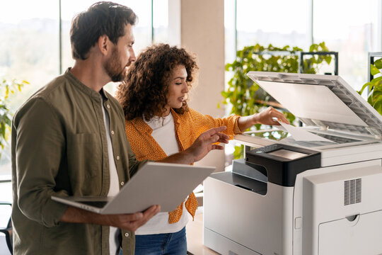 Business colleagues using printer in office with laptop