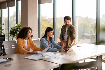 Marketing team analyzing data on laptop in modern office working together