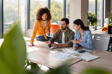 Group of focused colleagues collaborating on laptop in modern office