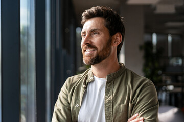 Fototapeta premium Smiling businessman looking out of window in office contemplating future success