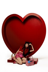 Trendy woman in red fur top and pink skirt lounging by a large red heart.
