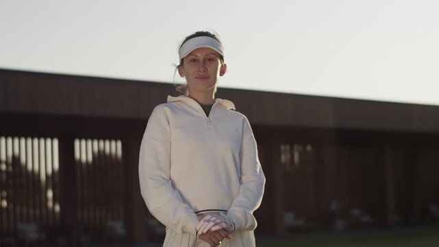 Pretty cheerful woman with visor hat leans onto golf club