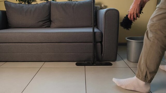 Man cleaning tiled floor with mop at home. Domestic lifestyle video of wringing mop cloth in bucket and starting to wash floor in cozy living room.