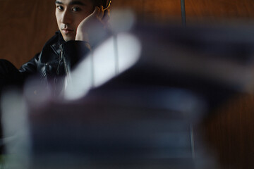 Young man in black leather jacket looking thoughtfully while sitting indoors.