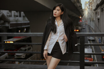 Stylish woman in a black blazer and white shirt poses confidently on an urban balcony.