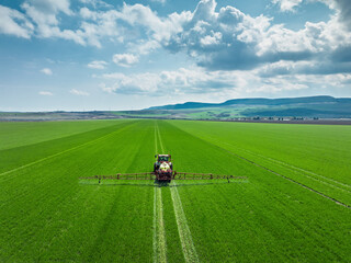 Aerial view of farming tractor plowing and spraying on fresh green wheat field