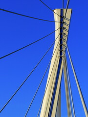 Close-up of a modern cable-stayed bridge tower with cables against a deep blue sky.