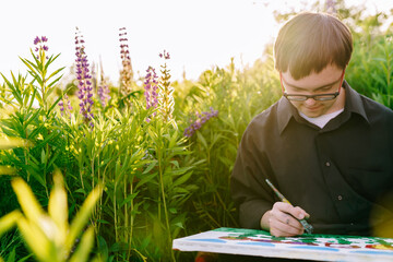 Boy with Down syndrome painting with brush in sunny meadow © Iryna