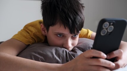 Closeup of a tired teenage boy lying on a pillow and watching a smartphone screen in a quiet bedroom at home. - Powered by Adobe