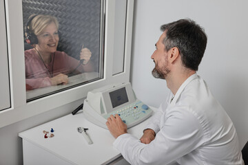 Obraz premium Audiological exam. Audiologist doing hearing check-up to mature woman in soundproof audiometric booth. Hearing loss treatment