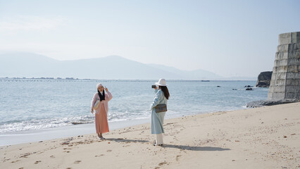 Two women in light summer clothing enjoying a beach day and taking photos.