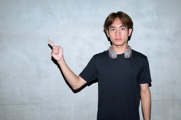 Young Thai man in black t-shirt near brutalist concrete wall in construction area pointing finger