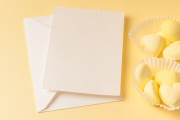 White paper tartlets with yellow marshmallows and a white envelope with a blank card on a creamy...