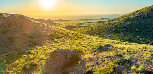 Sunset over green hills and valley, illuminated by the golden sunlight.