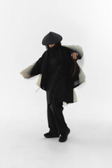 Fashionable figure in black outfit striking a dynamic pose in a minimalist setting.