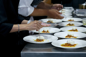 chefs in a professional kitchen garnishing dessert plates with precision. restaurant chef team showcasing fine dining presentation, culinary creativity, and teamwork in food preparation.