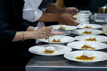 chefs in a professional kitchen garnishing dessert plates with precision. restaurant chef team showcasing fine dining presentation, culinary creativity, and teamwork in food preparation.