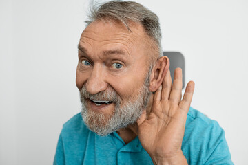 Old man with hearing problems in hearing clinic, hearing impaired and holding hand near ear to hear...