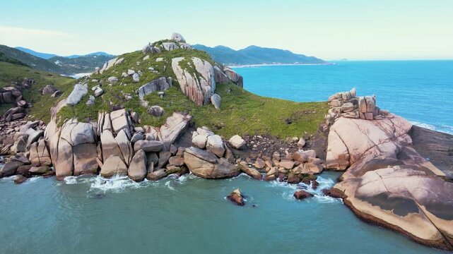 Aerial view of the rocky shore of Gravata Beach in Florianopolis, Santa Catarina, Brazil, with a dragon's head full of rocks, nature, and abundant Atlantic Forest with a turquoise ocean.