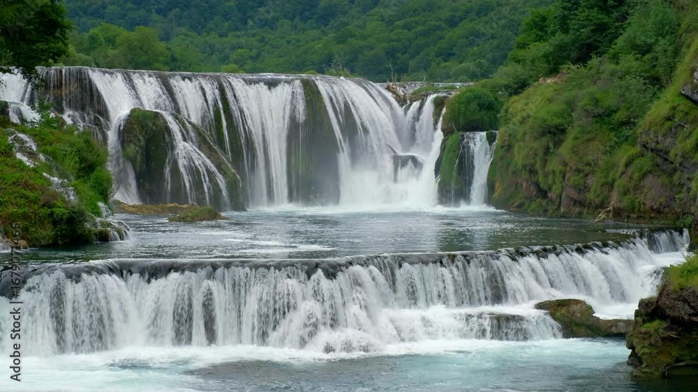 Poster waterfalls cascading down rocks create a natural scene with flowing water green trees are in the bac