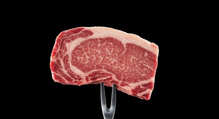 Marbled raw ribeye beef steak on fork showcases food photography concept for delicious gourmet meal against black backdrop