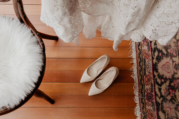 Bridal shoes under lace dress on wooden floor with vintage rug